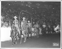[Group of cowboys entering rodeo arena on horseback]