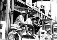 [Possibly Gene Autry sits on chute gate with other cowboys watching the action]