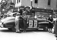 [Possibly Sally Rand leaning against automobile at a street corner advertising the rodeo]