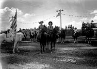 [Unidentified Cowboy & cowgirl on horses; cowgirl on pony to line of cowboys & cowgirls behind them]