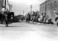 [Group of mounted cowboys moving down street in parade]