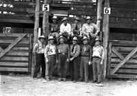 [Six cowboys standing in front of chute # 5 with an additional four cowboys sitting on chute gate]