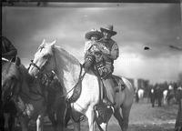 [Older cowboy with glasses on horseback holding child dressed in Mexican gear]