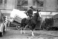 [Herman Linder posed on horse with horse trailers behind]