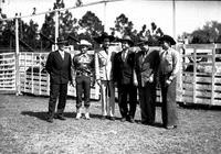 [Six men in line in front of cattle pens; Three in business attire, three in western wear]