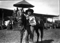 [Possibly Johnny Jordan  wearing tie, "JJ" on shirt standing by horse with silver mounted bridle]