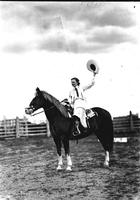 [Unidentified cowgirl raising hat above head on horse]