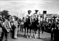 [Autry on horseback with mounted cowboy alongside; Spectators including many young boys at sides]