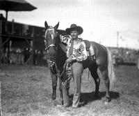 [Possibly Johnny Jordan in satin shirt standing with horse in silver mounted bridle & breast collar]