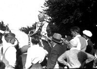 [Hatless unidentified cowboy atop horse signing autographs surrounded by men and boys]