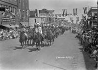 [Mounted Indian men parading down spectator lined street]
