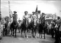 [Autry on horseback flanked by other mounted cowboys bearing flags]