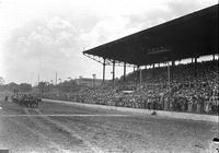 [Photograph of Rodeo performers lined up on track in front of spectator packed grandstand]