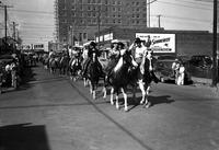 [Pairs of riders, mostly cowgirls, moving down street]