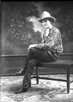 [Young unidentified Cowboy sitting on bench and wearing rose-print shirt, a scarf, and white hat]