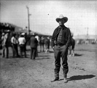 [Unidentified Cowboy standing with hands in pockets group of cowboys in background]