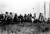 [Group of eight cowgirls and cowboys on horseback in tall grass]