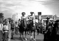 [Autry on horseback with mounted cowboy alongside; Spectators including many young boys at sides]