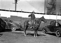 [Unidentified cowboy in plaid coat atop horse holding a rope loop to his side]