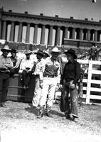 [Autry standing with unidentified man (F? on chaps), Cowboys and clowns in background]