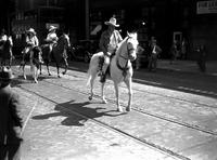 [Unidentified Cowboy on horse followed by mounted cowboys parading down trolley car tracks]