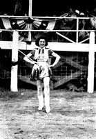 [Unidentified majorette holding baton and posed in front of bandstand]