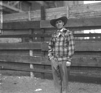 [Possibly Tex Sherman in Plaid Wool Jacket, Neckerchief, and Hat in front of fence]