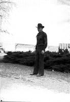 [Unidentified cowboy standing in front of low bush line]