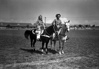 [Unidentified Cowboy and Cowgirl mounted on horses, her horse wearing splint boots and leg wraps]