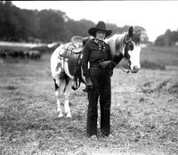 [Unidentified cowgirl standing beside horse]