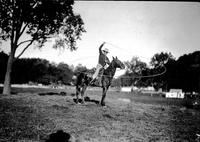 [Unidentified Cowboy sitting atop stationary horse spinning a large rope loop around himself]