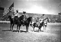 [Three unidentified cowboys on horseback, one carrying American Flag and one young cowboy on a pony]
