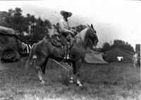 [Tom Mix wearing buttons on lower leg of pants on horse with silver mounted tack]