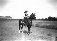 [Unidentified cowgirl posed on horse on racetrack]