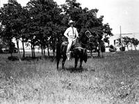 [J. Wills on dark horse wearing silver saddle. Trees and Stadium in background]