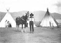 [Unidentified cowgirl by horse with tipis in background]