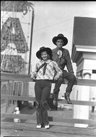 [Unidentified cowgirl and cowboy leaning & sitting on railing]