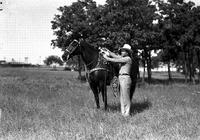 [J. Wills standing beside dark horse wearing silver saddle.  Trees in background]