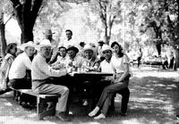 [Gene Autry and group of cowboys and women sitting at picnic table in park]