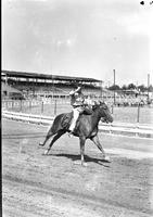 [Unidentified cowboy on galloping horse on track holding hat with right hand]