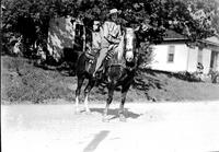 [Unidentified cowgirl on horse with house in background]