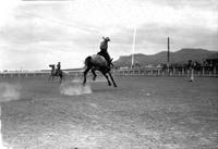 [Unidentified Cowboy riding and staying with Saddle bronc with distant hills in background]