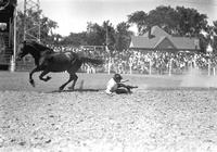 [Unidentified Cowboy in dirt on his right hip & elbow as his mount gallops away in front of stands]