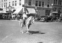 [Unidentified cowgirl on horse in street, apparently part of a parade]