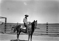 [Young cowboy on horseback in front of pole fence]