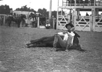 [Unidentified cowboy sitting on ground with back supported by lying horse's belly]