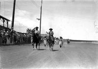 [Unidentified Cowboy tipping hat to crowd & cowgirl with quirt riding beside]