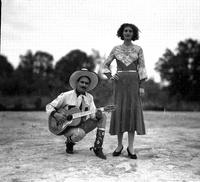 [Possibly Jack Wolfe with guitar kneeling & Marie Wolfe standing by him in heels & decorative dress]