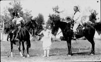 Two cowboys on horses, cowgirl on foot