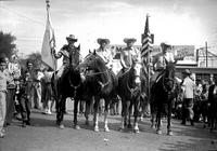 [Autry on horseback flanked by other mounted cowboys bearing flags]